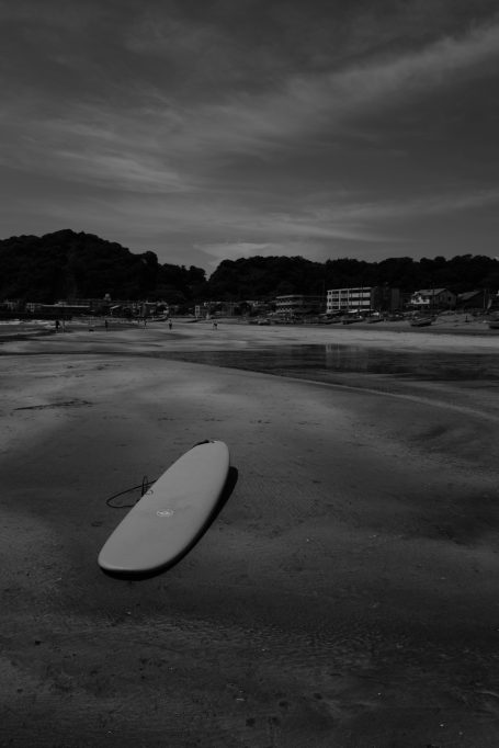 Ein einsames Surfbrett liegt am kühlen Strand unter bewölktem Himmel.