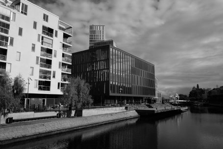 Moderne Gebäude am Kanal, umgeben von Wasser und Bäumen, in Schwarz-Weiß.