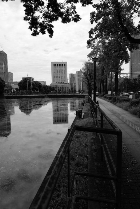 Städtische Uferpromenade entlang eines ruhigen Flusses mit reflektierenden Gebäuden.